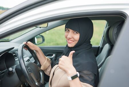 Beautiful arab muslim woman driving car and showing thumbs up outdoor