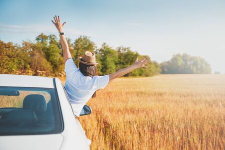 Young woman with hands raised in white car on the field outdoorの写真素材