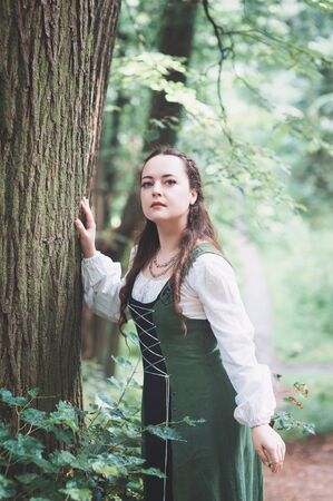Beautiful woman in green medieval dress near tree outdoor