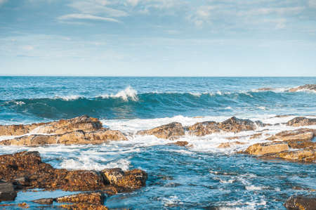 Sea waves crashing on rocks in sunny day