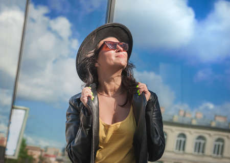 Beautiful young happy woman with hair flying in the wind near the mirror wall of city buildingの写真素材