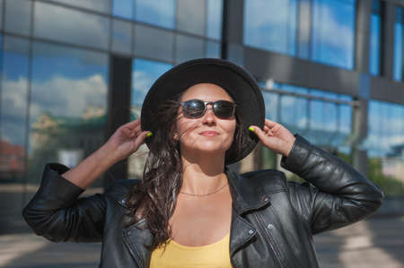 Beautiful young happy woman with hair flying in the wind near the mirror wall of city buildingの写真素材