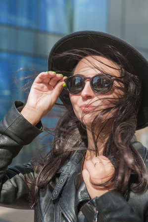 Beautiful young happy woman with hair flying in the wind near the mirror wall of city building