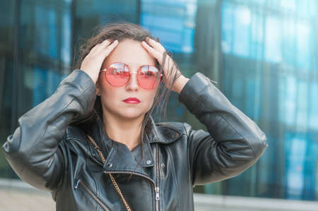 Beautiful young woman with pink sunglasses on the mirror wall of city building background