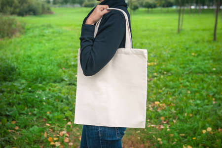 Stylish woman holding white blank canvas tote shopping bag outdoorの写真素材