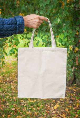 Stylish man hand holding white blank canvas tote shopping bag outdoorの写真素材