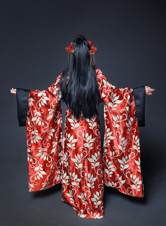 Beautiful young woman back pose in red traditional Chinese costume on dark backgroundの写真素材