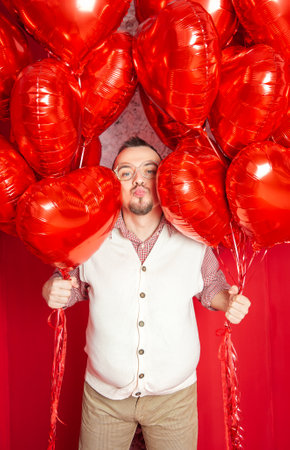 Funny happy bearded retro style man in the white vest with red heart shape balloons sending kiss for Valentine dayの写真素材