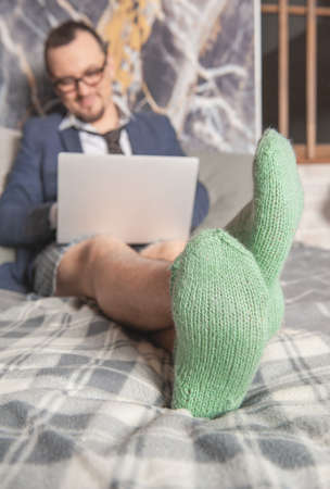 Young handsome man wearing suit and underpants in the green socks working at home online sitting on the bed. Focus on the socksの写真素材