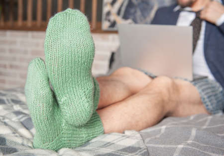 Young handsome man wearing suit and underpants in the green socks working at home online sitting on the bed. Focus on the socksの写真素材