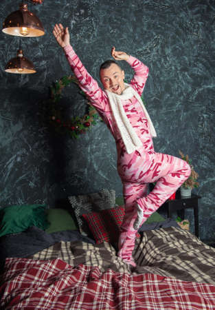 Cheerful funny happy man in pink sleepwear dancing on bed in Christmas timeの写真素材