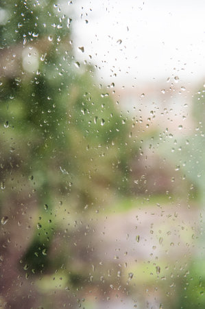 Rain drops on the window with blurred green trees in background. autumn concept