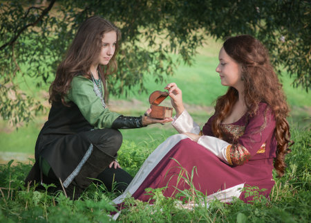 Young beautiful couple in medieval style dresses sitting on the grass outdoor in summer