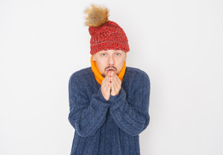 Young handsome man wearing in red hat and blue pullover feeling cold on white background. gas crisis conceptの写真素材