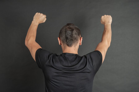 Young man with hands raised up protest gesture back pose on dark backgroundの写真素材