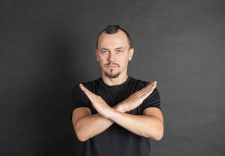 Young handsome man showing X sign hands gesture on dark backgroundの写真素材