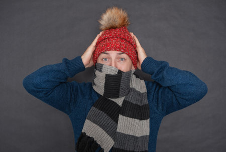 Frightened young handsome man wearing in red hat and blue pullover feeling cold on dark background. gas crisis conceptの写真素材