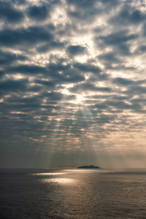 Beautiful landscape with Sun beams breaks through dark clouds over sea waterの写真素材