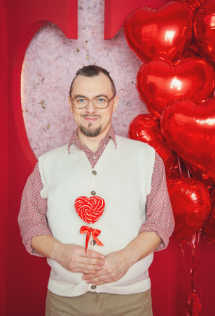 Funny bearded retro style man in the white vest holding red heart shape lollipop for Valentine's dayの写真素材