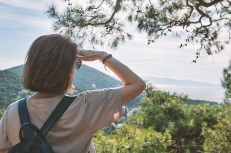 Woman with backpack looking at beautiful scenic view at hills and sea waterの写真素材