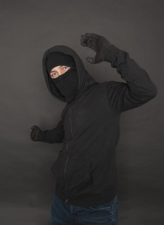 Unrecognizable man in the black hoody with hood wearing balaclava mask up with hand on dark...