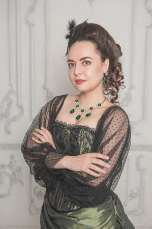 Beautiful young smiling woman wearing green medieval vintage Victorian Style dress stand in the roomの写真素材