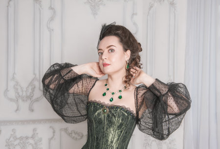 Portrait of Beautiful young woman wearing green medieval vintage Victorian Style dress in the room