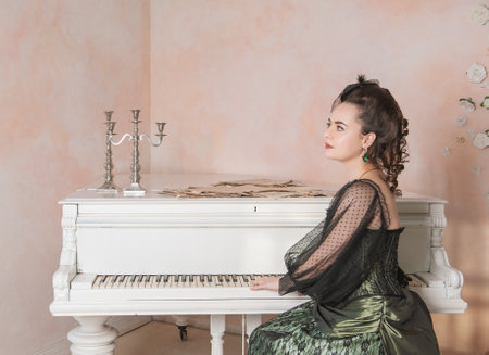 Beautiful young thoughtful woman wearing green medieval vintage Victorian Style dress sitting near...