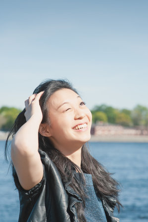 Beautiful young woman with long black hair smiling in the city at sunny dayの写真素材