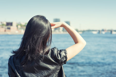 Young woman with long black hair looking at the water in the city. back pose