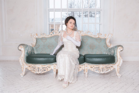 Beautiful young woman wearing medieval vintage Edwardian Style dress sitting on the sofa