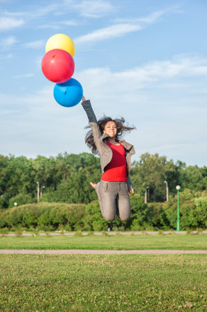 Young beautiful happy business woman with long hair jumping with air balloons outdoor in the city parkの写真素材