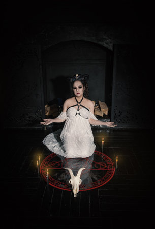 Beautiful woman witch with horns wearing white lacy dress making Halloween ritualの写真素材