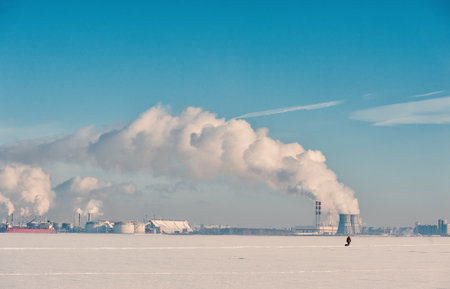 Winter landscape with snow covered frozen ice, city and pipes with thick steamの写真素材