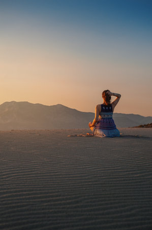 Silhouette of beautiful woman sitting on the sand against sunrise sky and mountainsの写真素材