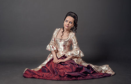 Young beautiful woman in rococo style medieval dress sitting on the floor against dark backgroundの写真素材