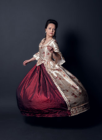 Young beautiful smiling woman in rococo style medieval dress dancing against dark backgroundの写真素材