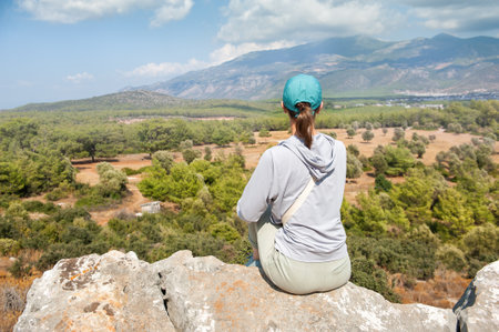 Beautiful tourist woman sitting on the ancient ruins in Antalya Province, Turkey, back poseの写真素材