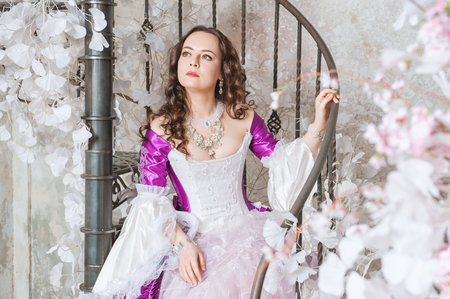 Young beautiful woman in fantasy white and purple rococo style medieval dress sitting on the...