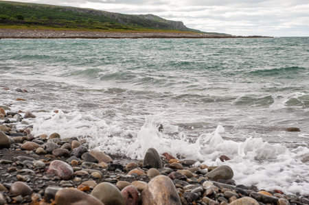 Sea waves in storm, big stones on the shore and green hill