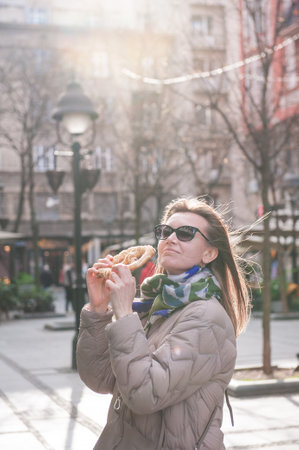 Beautiful young woman having fun with bagel outdoor on the street in Belgrade, Serbiaの写真素材