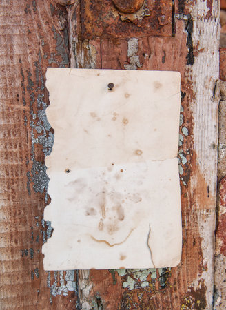 Old vintage paper advertisement hanging on aged wooden wall nailed by rusty doornailの写真素材
