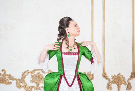 Young beautiful woman in green rococo style medieval dress turn standing near wall