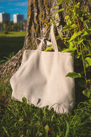 White canvas tote bag mockup template with long handles among the green plant leaves outdoor....