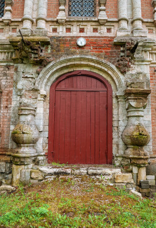 Weathered red door framed by an arched stone entrance showcases vintage architectureの写真素材