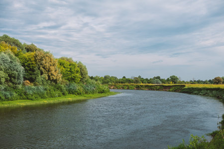 Idyllic view of a calm, rural scene with a wide river reflecting the peaceful, verdant greenery of the countrysideの写真素材