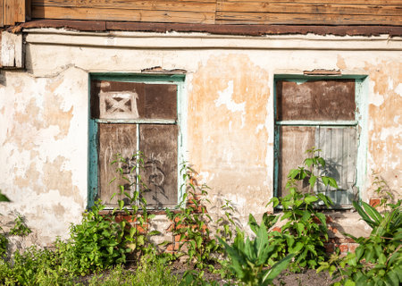 Weathered cement wall of an abandoned house with boarded up windows shows signs of decay. Rustic, aged planks display peeling paint and cracksの写真素材