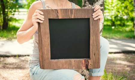 Woman holding empty blackboard with wooden frame outdoor. Template Mockupの写真素材