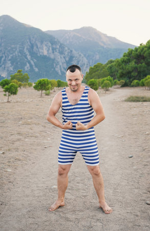 Man flexes in a vintage striped swimsuit, posing confidently outdoors with a playful smileの写真素材