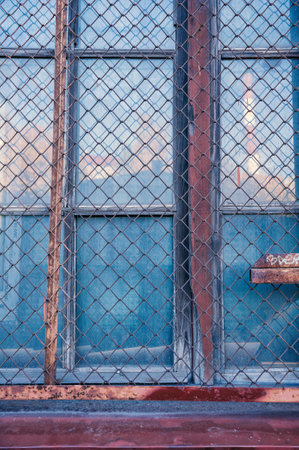 Rusted metal grid guards a weathered glass window in an old, decaying structureの写真素材